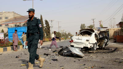 En afghansk soldat promenerar förbi ett söndersprängt bilvrak