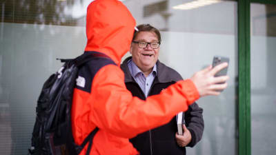 En ung person i orange jacka tar en selfie med Timo Soinin i ett köpcenter i Ivisnäs.