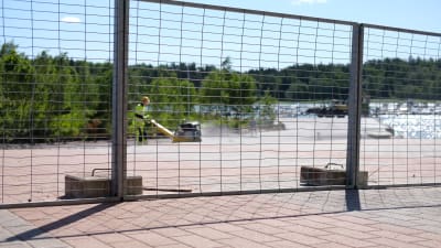 En man packar sand med en maskin bakom ett metallstaket.
