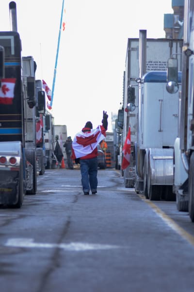 Demonstrant med Kanadas flagga över axeln går mellan långtradare på en gata i Ottawa.
