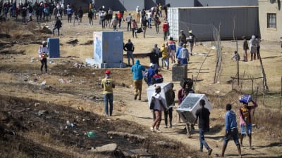 Invånare i Soweto utanför Johannesburg bär hem varor, som ugnar och kylskåp, som plundrades från en närliggande varuhus.