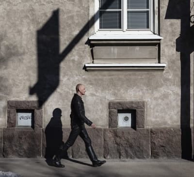 Nahkavaatteisiin pukeutunut mies kävelee harmaaseinäisen rakennuksen ohitse.