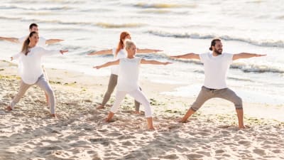 Grupp som yogar i vita kläder på en strand
