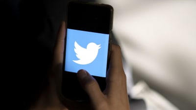 Twitters logotyp med en vit fågel mot en blå bakgrund visas på en mobiltelefons skärm.