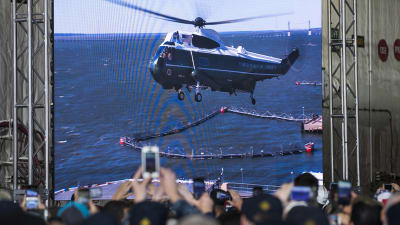 En folkhop följer med när Donald Trumps helikopter anländer till hangarfartyget för att hålla presskonferens.