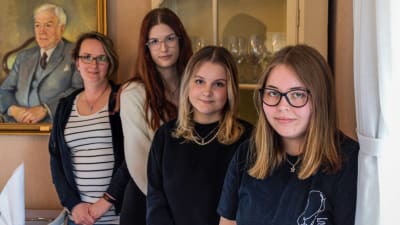Fyra unga kvinnor poserar vid ett hörnskåp i en restaurang. 