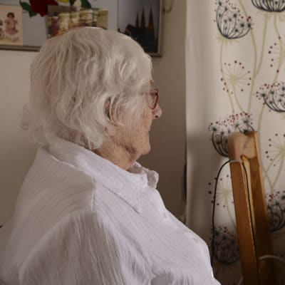 Äldre kvinna i profil som sitter vid ett fönster.