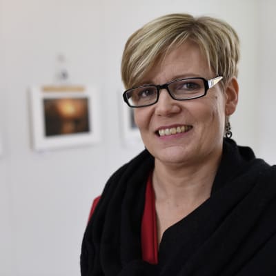 Tina Nylund ler mot kameran med foton i bakgrunden.