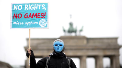 En person i blå mask protesterar mot vinter OS i Peking och Kinas behandling av Uigurer genom att hålla upp en blå skylt med texten "No Rights, No Games" framför Bradenburger Tor i Berlin. 