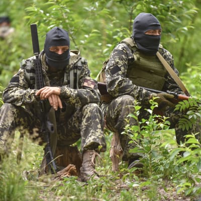 Två ukrainska soldater klädda i full utrustning sitter i en skog.