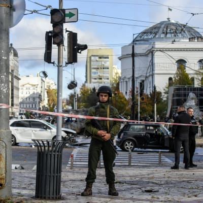 Beväpnad man klädd i grönt framför förödelse i Ukrainas huvudstad Kiev efter ryska robotangrepp 10 oktober 2022. 