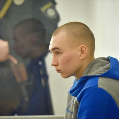 En bild av Vadim Sjisjimarin. I bakgrunden syns en vakt med ett automatvapen.