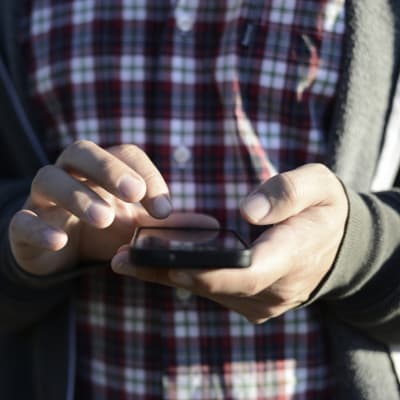 En person håller en smarttelefon i handen och håller fingret ovanpå skärmen.