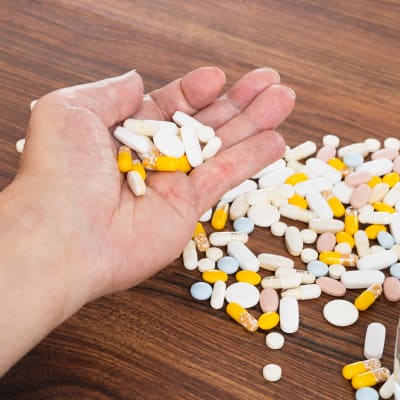 En hand full med piller ovanför ett träbord.