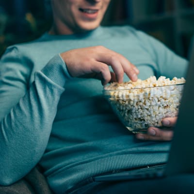 Man tittar på film på laptop och äter popcorn