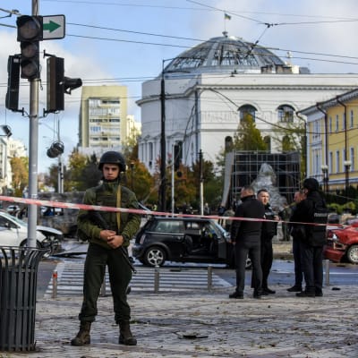 Beväpnad man klädd i grönt framför förödelse i Ukrainas huvudstad Kiev efter ryska robotangrepp 10 oktober 2022. 