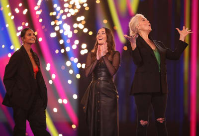 Tre kvinnor, alla klädda i svart, står på en scen.