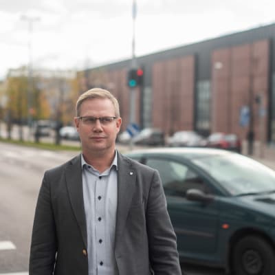 Direktören för den svenska servicehelheten vid sektorn för fostran och utbildning, Niclas Grönholm, står ute framför en väg. Det är höst. En bil kör förbi, Grönholm ser allvarsam ut och tittar åt höger.