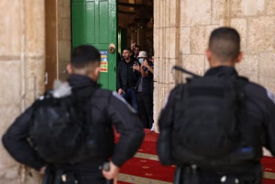 Palestinier tittar ut genom dörren i al-Aqsamoskén i Jerusalem, israelisk polis bevakar byggnaden.