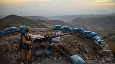 En turbanförsedd milisman står bakom en maskingevär i bergig terräng