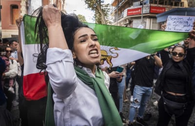 En kvinna drar sig i håret under en demonstration medan hon ropar. I bakgrunden Irans flagga.