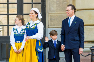 Prinsessan Estelle och kronprinsessan Victoria ler mot publiken, prins Oscar vinkar ena handen och håller i pappa prins Daniel med den andra.