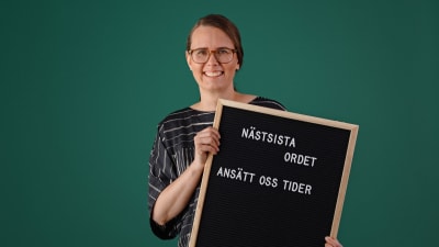 Jenny Sylvin håller i en svart tavla med texten "Näst sista ordet, ansätt oss tider".