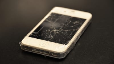 Telefon med sprucken skärm ligger på ett bord.