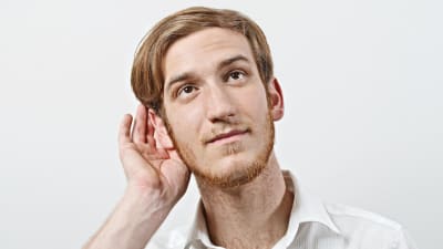 En man håller sig bakom ena örat och lyssnar uppmärksamt.