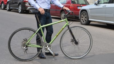En grön cykel. En man håller i cykeln, endast hans nedre kropp syns i bild.