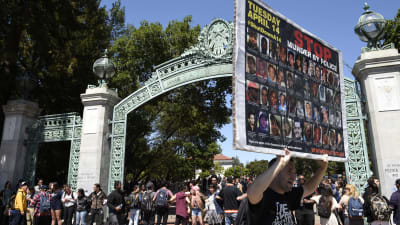 Demonstranter står utanför en ingång till universitetsområdet i Berkeley och håller upp ett plakat med tiotals svarta ansikten och texten "Stoppa mord utförda av polisen".