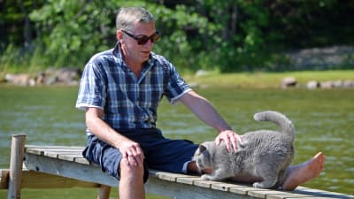 Peter Oljemark sitter på en brygga och klappar katten Oscar.