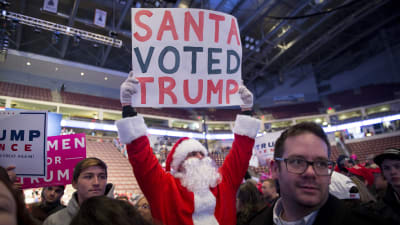 En man utklädd till jultomten håller upp en skylt"Jultomten röstade på Trump"