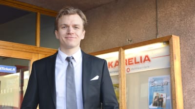 Alfred Backa, iklädd kostym står utanför dörren till kulturhuset Karelia i ekenäs. 