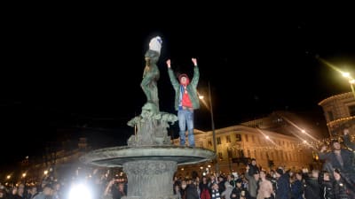 En man står på statyn Havis Amanda med armarna uppsträckta i luften.