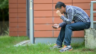 En man sitter med en mobiltelefon i handen utanför en flyktingförläggning i Sigmaringen i Tyskland.