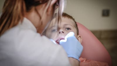 En tandläkare tittar in i munnen på ett barn