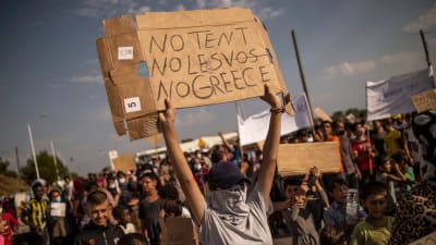 Flyktingar och migranter från det nedbrunna Moria-lägret demonstrerade på fredagen mot planerna på ett nytt läger. Nej till tält, Lesbos och Grekland, står det på ett av plakaten. 