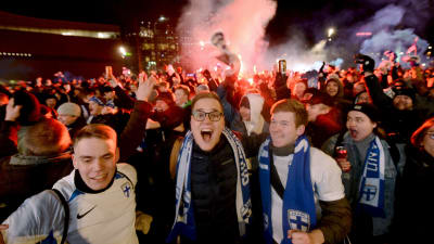 Många fans som firar, tre stycken glada män i förgrunden med matchhalsdukar i Finlands färger.