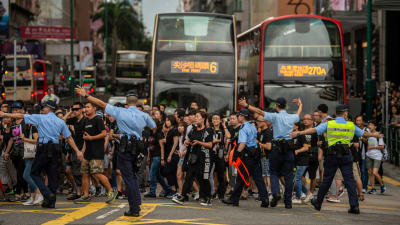 Demonstranter korsar en väg i hongkong. Polis visar riktningen.