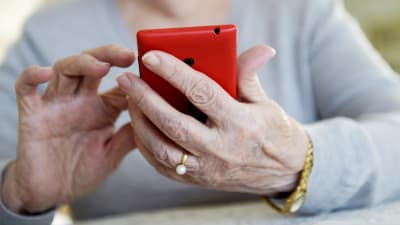 En äldre kvinna håller en röd smarttelefon i handen.