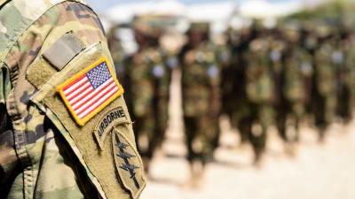 I förgrunden syns en soldats arm varpå man ser USA:s flagga på uniformen. I bakgrunden syns ännu fler soldater i uniform i Somalia.