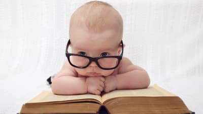 Bebis med glasögon som ligger på en bok och funderar.