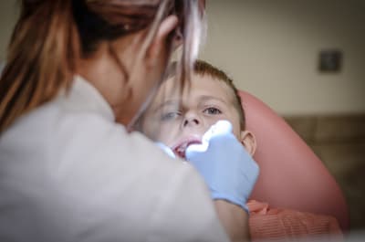 En tandläkare tittar in i munnen på ett barn