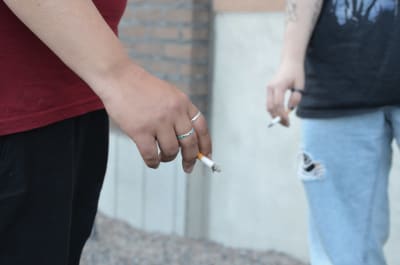 Närbild på två personers händer, de håller i cigaretter.