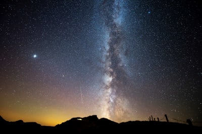 La Via Lattea e una stella cadente appaiono nell'oscuro cielo della sera.