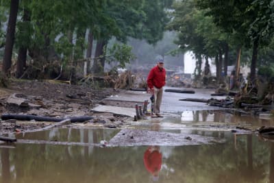 En man på en gata som inte längre finns för den är täckt av vatten och bråte efter översvämningen.