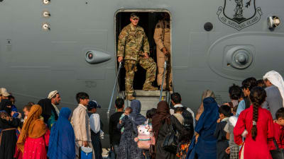 En amerikans soldat går ut ur ett militärplan. Framför honom står människor som väntar på att bli evakuerade från Afghanistan. Bilden är tagen på en militärbas i Qatar.