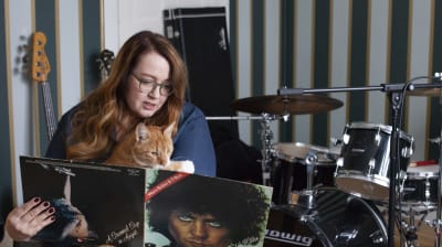 Jutta Carpelan sitter med sin katt i famnen och tittar på en vinylskiva.