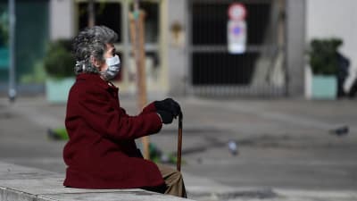 En kvinna i skyddsmask satt i centrum av ett rätt folktomt Milano på söndagen. 